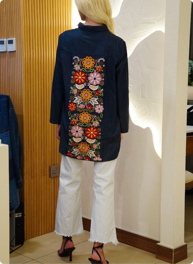 Denim blue in sturdy washed cotton shirt with collar and button down front and high low hem with embroidery at the back