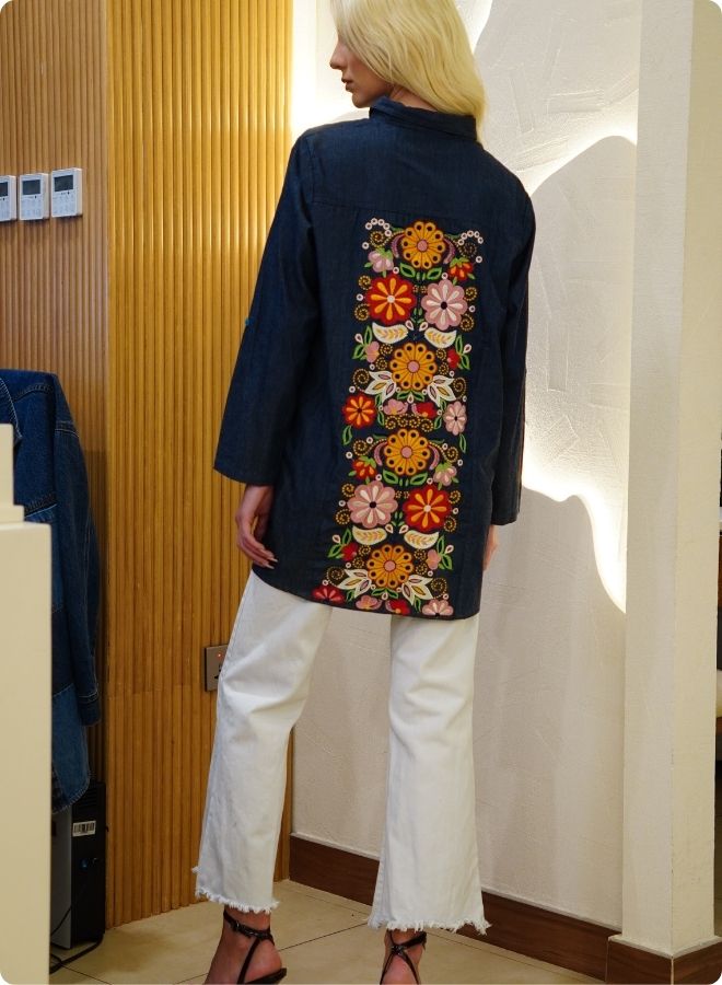 Denim blue in sturdy washed cotton shirt with collar and button down front and high low hem with embroidery at the back