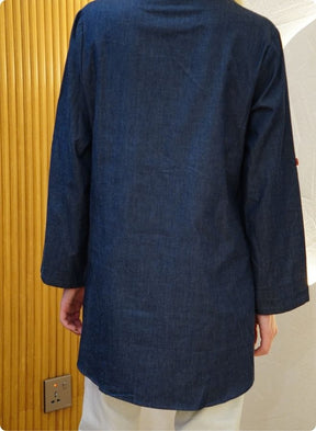 Denim blue in sturdy washed cotton shirt with collar and button down front and high low hem with embroidery at the back