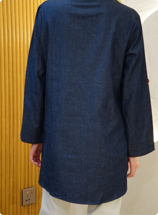 Denim blue in sturdy washed cotton shirt with collar and button down front and high low hem with embroidery at the back